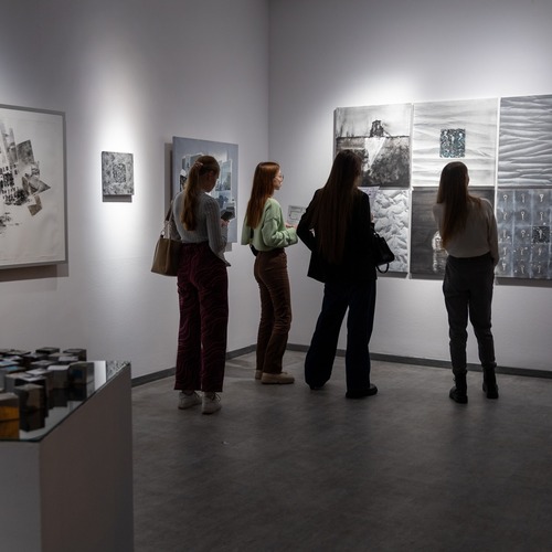Grupa młodych kobiet ogląda czarno-białe prace na ścianach galerii.