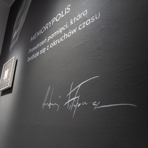 Napis na ścianie „MEMORYPOLIS. Przestrzeń pamięci, która buduje się z okruchów czasu” oraz podpis Andrzeja Filipowicza.
