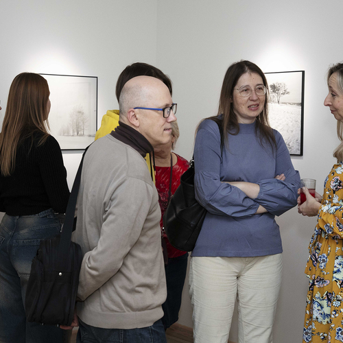 Grupa osób, w tle dwie, czarno - białe fotografie przedstawiające drzewa.