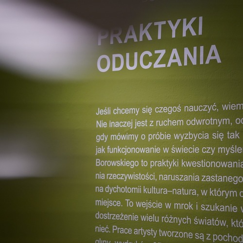 Zbliżenie na zieloną ścianę ekspozycyjną z białym tekstem kuratorskim zatytułowanym „Praktyki oduczania”..jpg